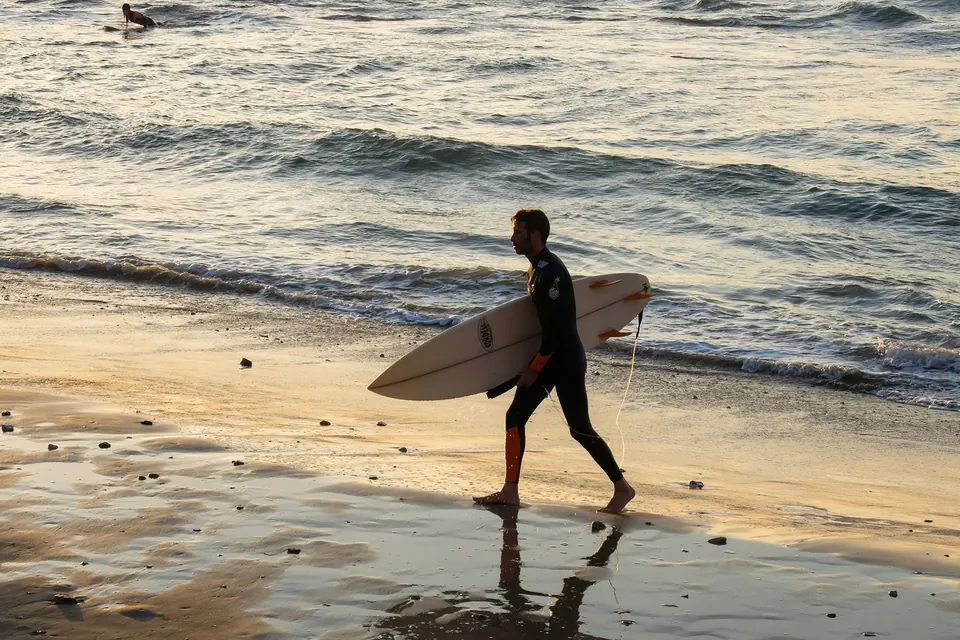 Before: a surfer carrying a board along the beach at sunset
